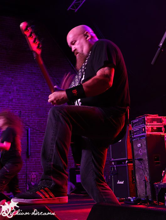 A guitarist energetically performing on stage at the Nile Theater, surrounded by amplifiers and colorful stage lighting.