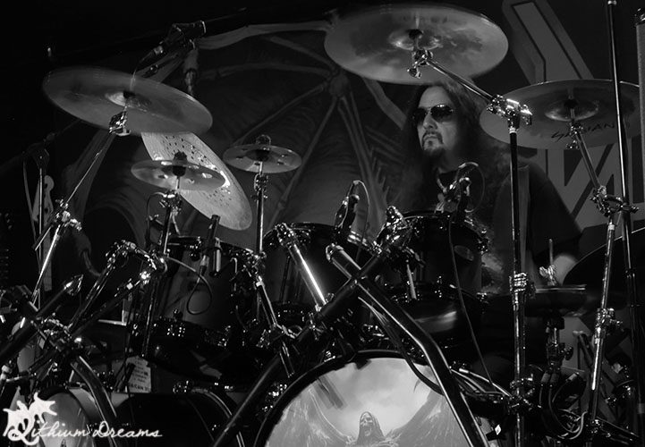 A drummer performing on stage in a thrash metal concert, captured in black and white.