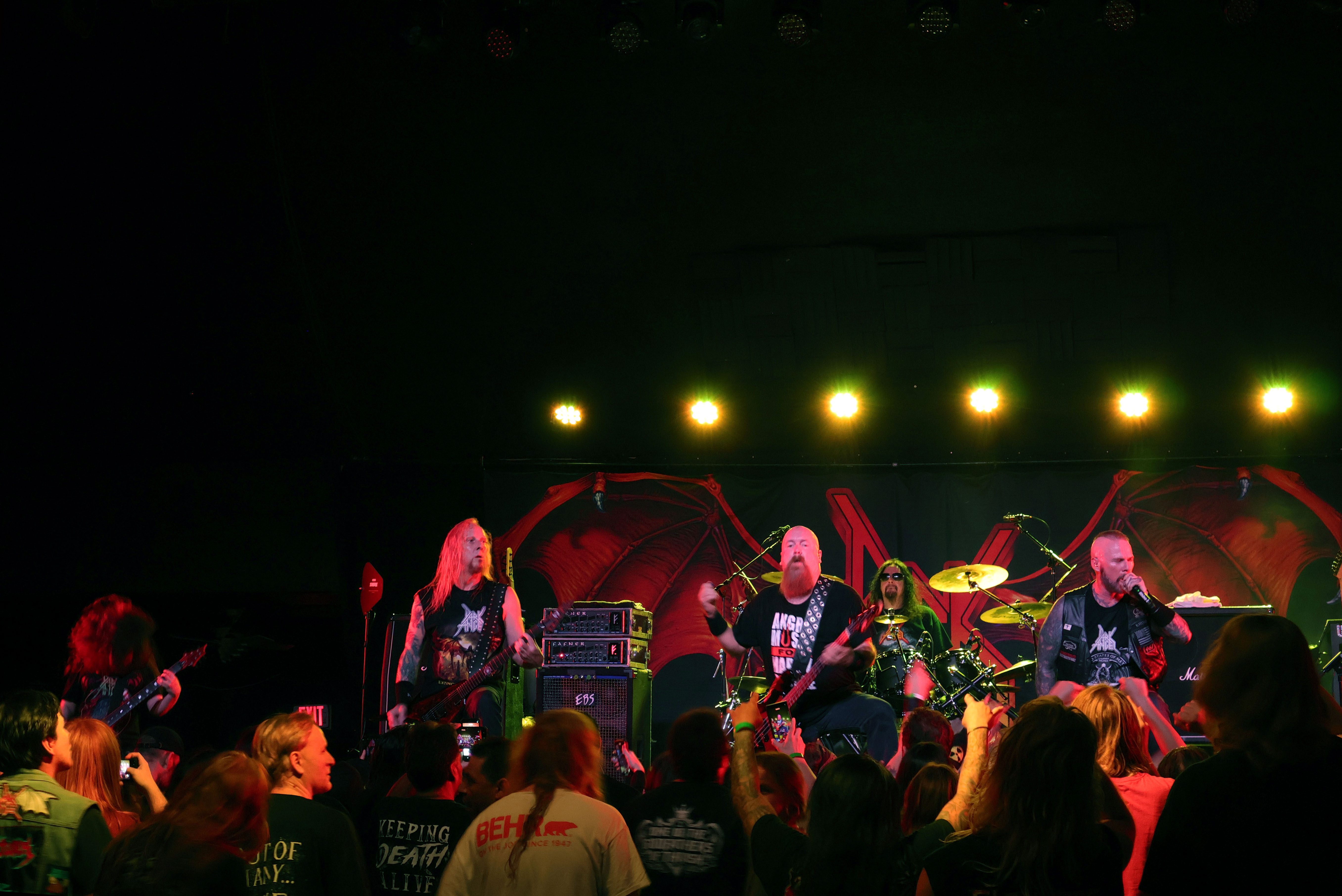 A thrash metal band performing on stage at the Nile Theater, surrounded by an energetic crowd.