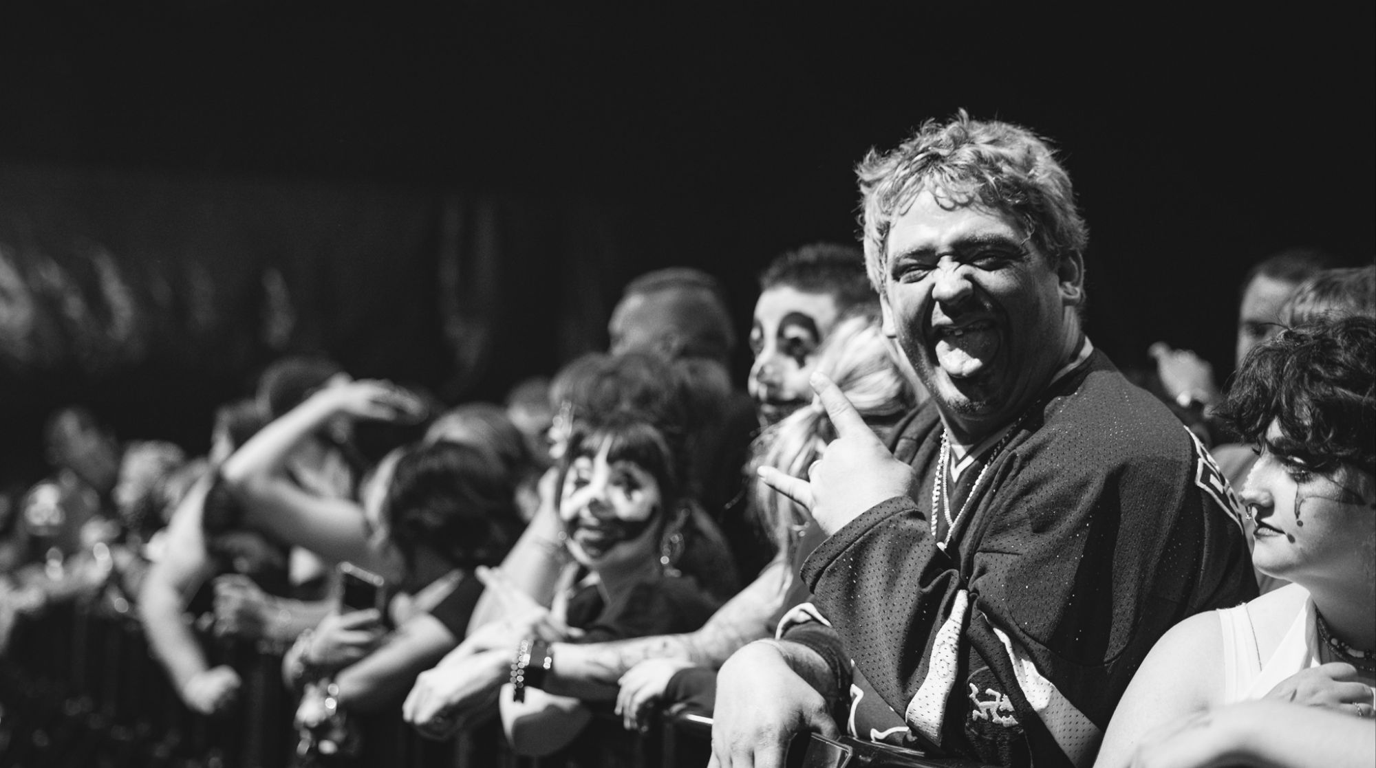 An enthusiastic crowd of Juggalo fans at a concert, some with face paint and expressions of excitement, enjoying the performance.