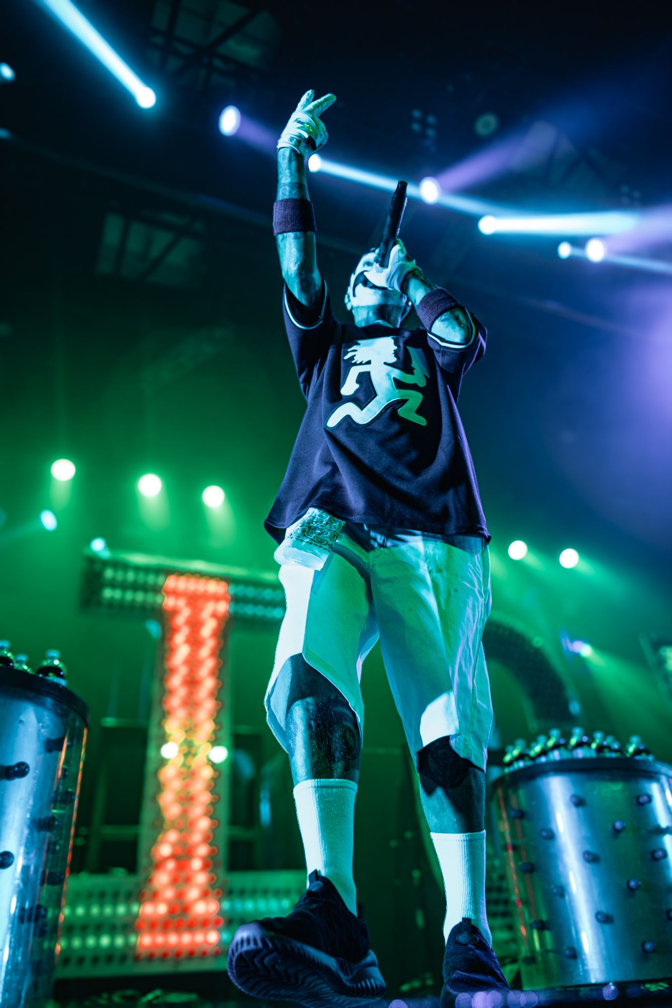 A performer from Insane Clown Posse on stage, passionately singing into a microphone with vibrant green stage lights in the background.