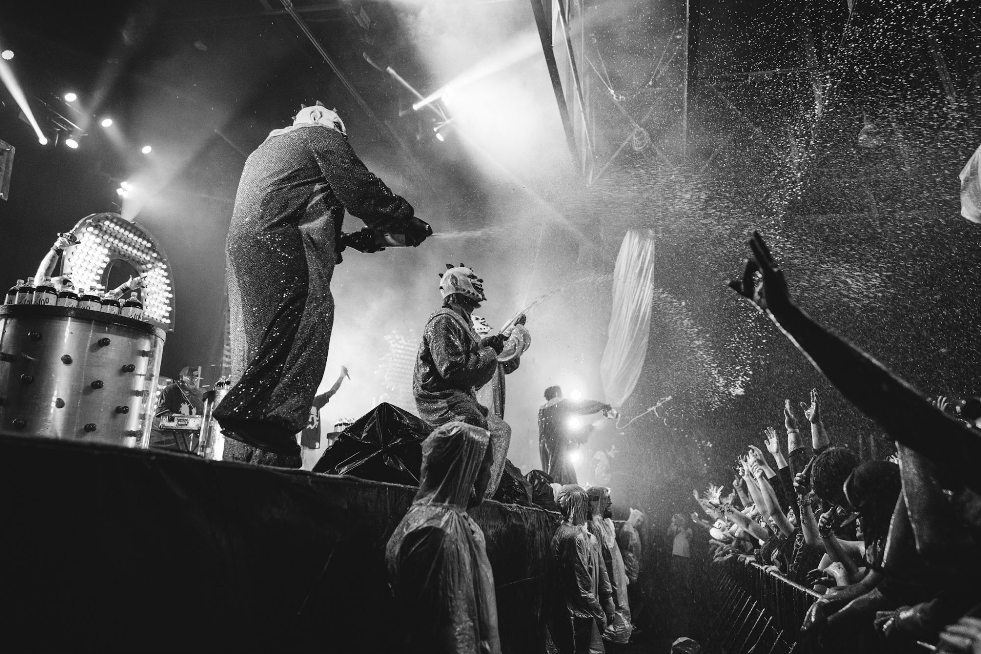 Insane Clown Posse performing on stage, surrounded by fans reaching out with enthusiasm, during a lively concert. The scene captures performers in colorful costumes and a mist of spray, creating a dynamic atmosphere.