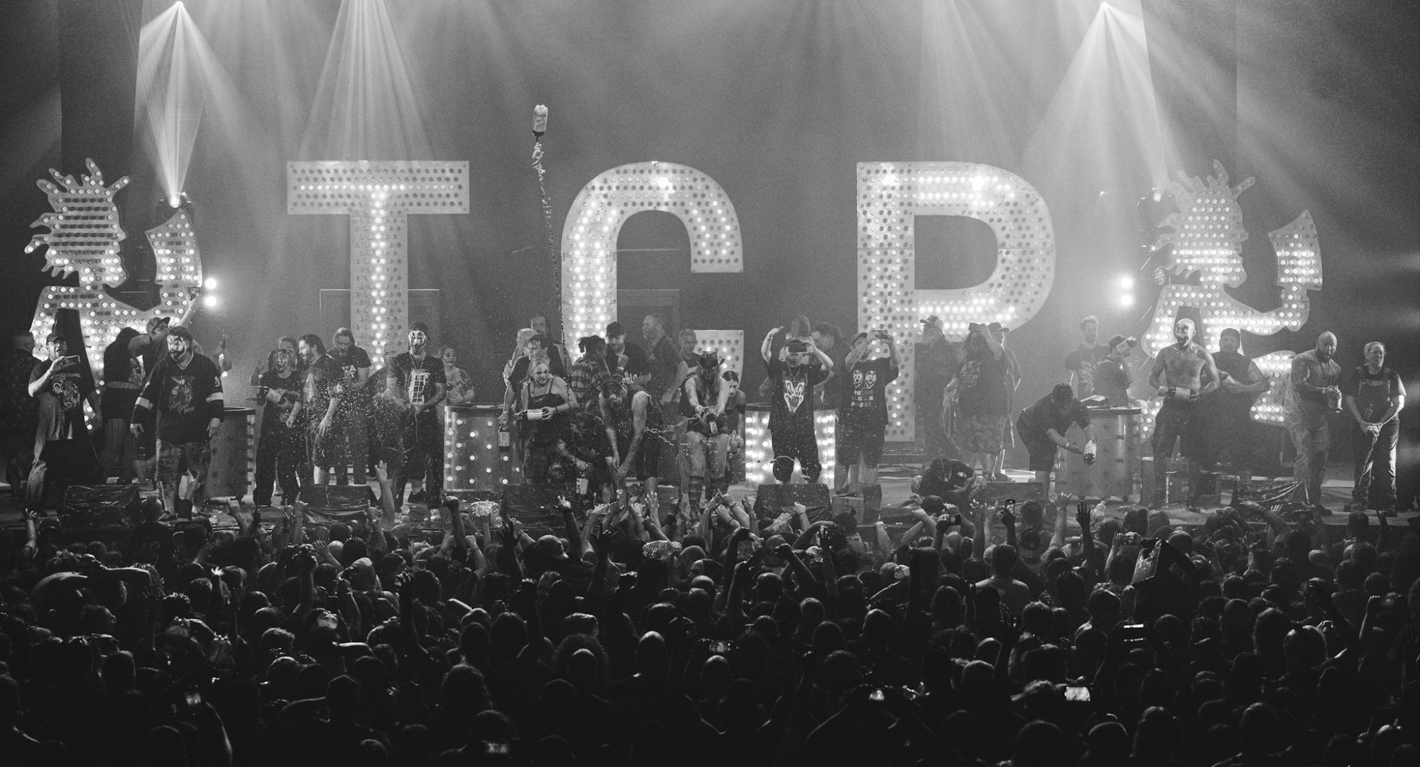 A lively performance by Insane Clown Posse on stage with a large crowd below, featuring bright lights and the iconic letters 'ICP' illuminated in the background.
