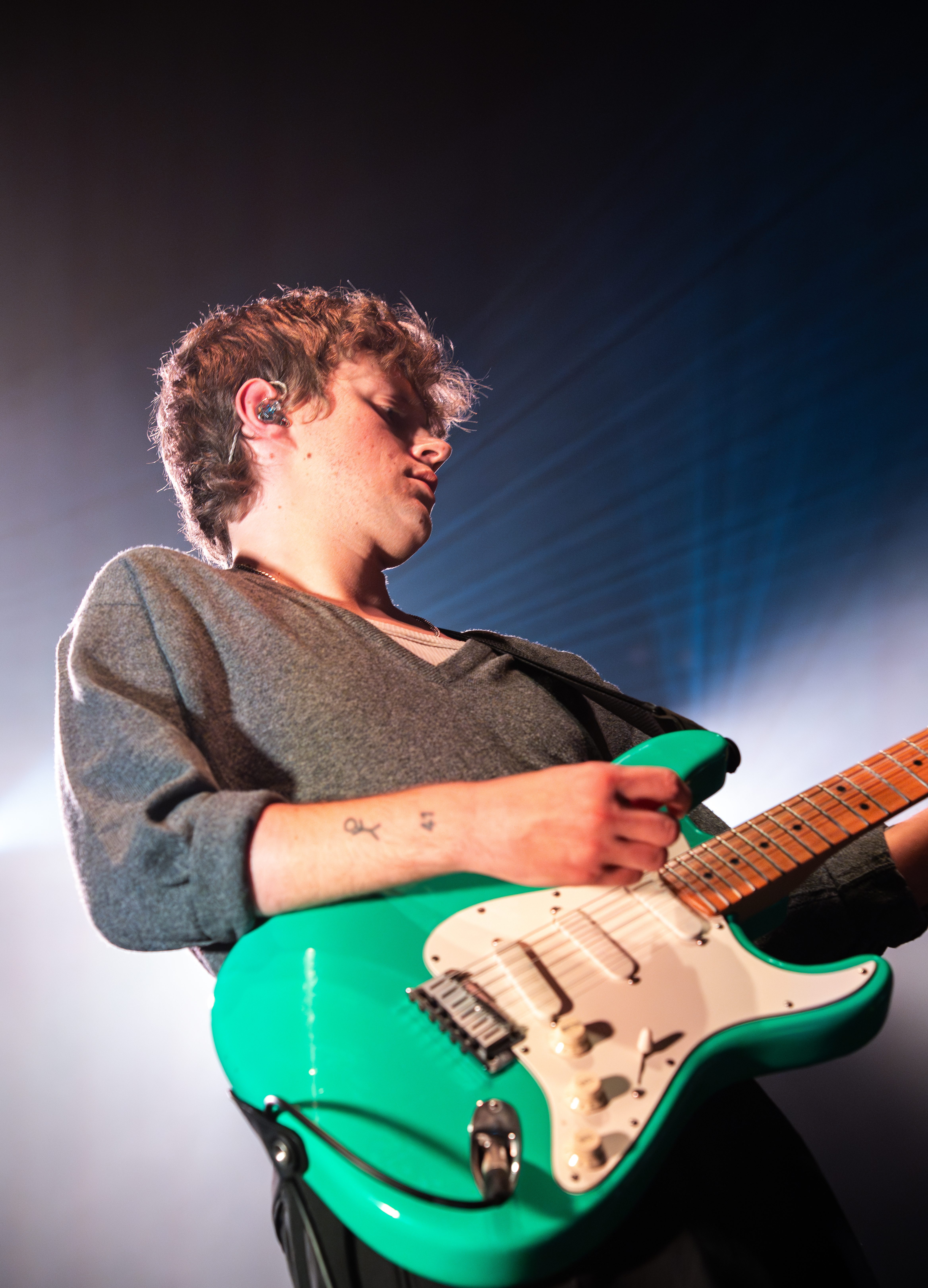 A musician passionately playing a green electric guitar while performing on stage, with dramatic lighting effects in the background.