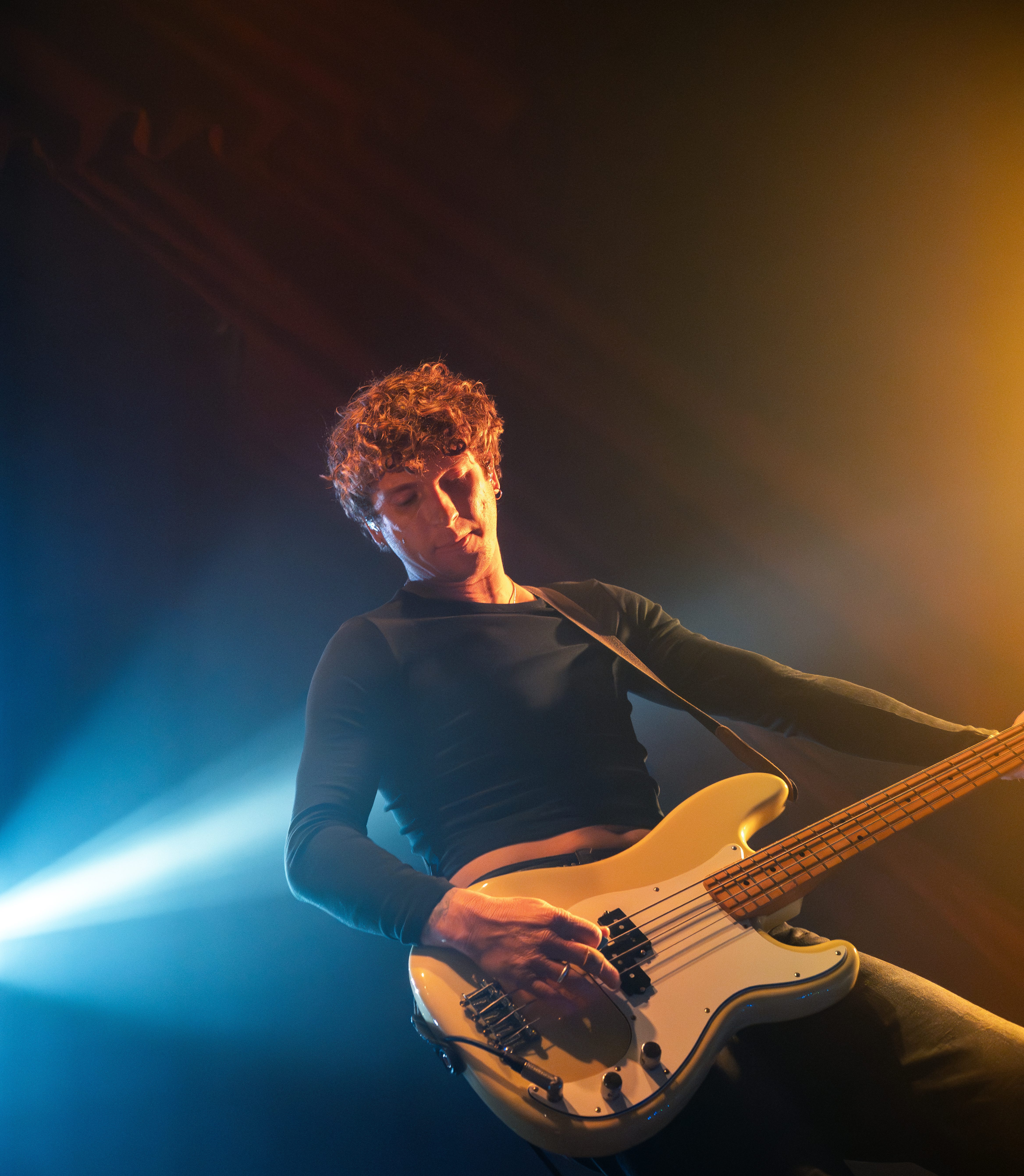A musician performing on stage, playing a bass guitar under colorful stage lights.