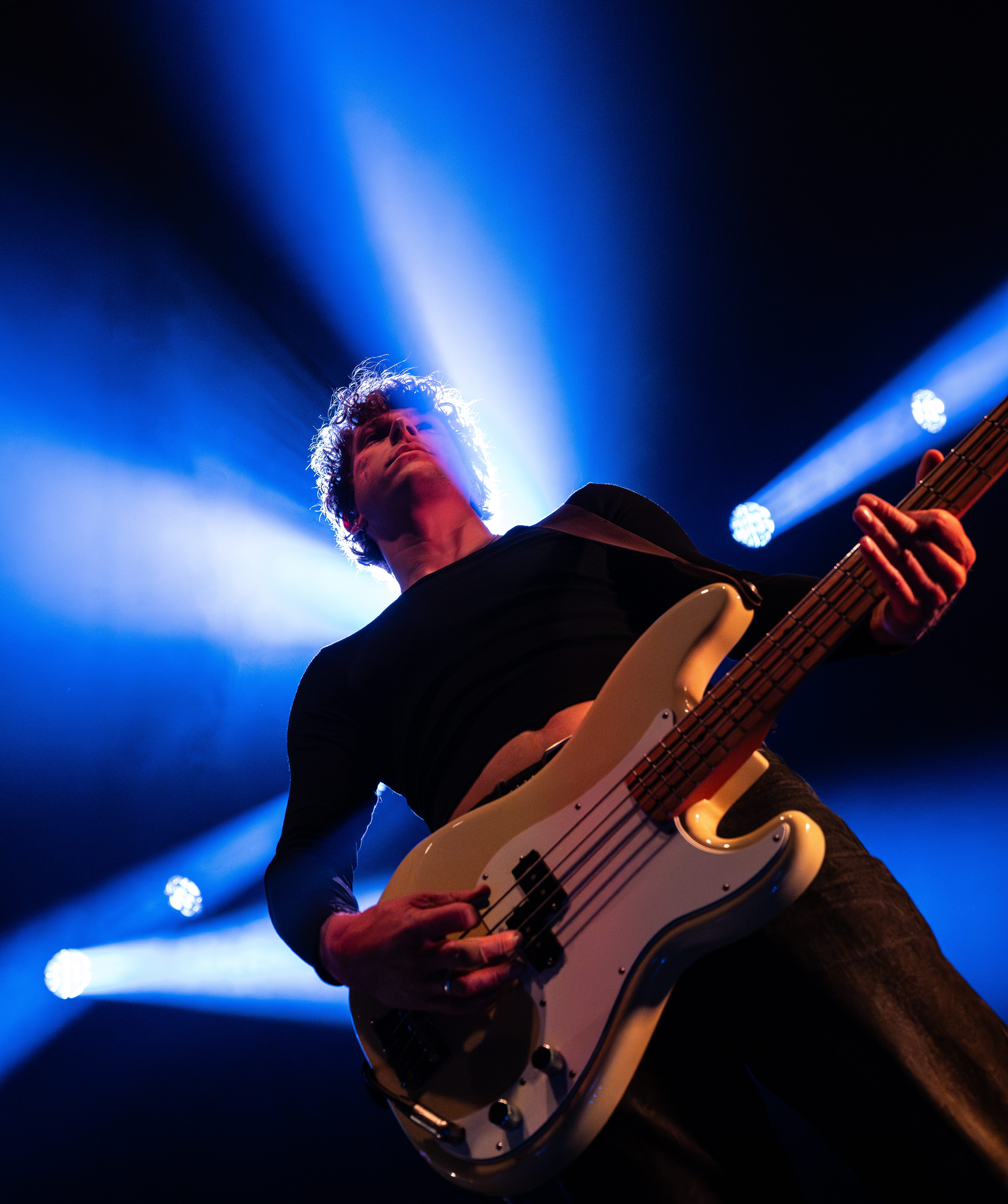 A musician playing an electric bass guitar on stage under dramatic blue lighting.
