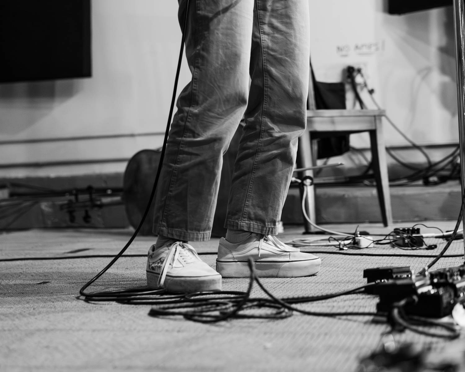 Close-up of a musician's feet wearing white sneakers standing onstage surrounded by microphone cables and instruments.