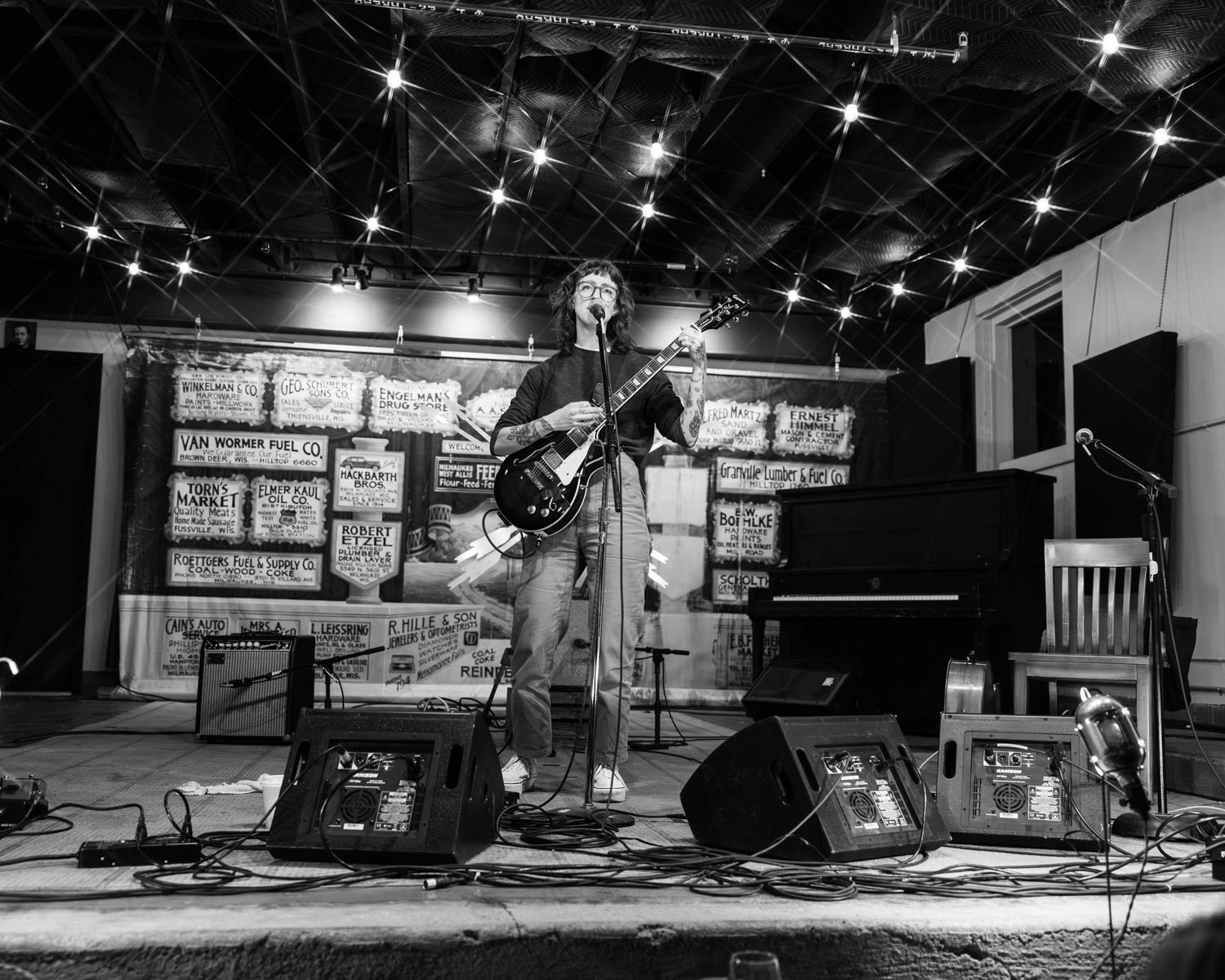 A musician performing on stage with an electric guitar in a cozy venue, surrounded by musical equipment and a vintage backdrop.