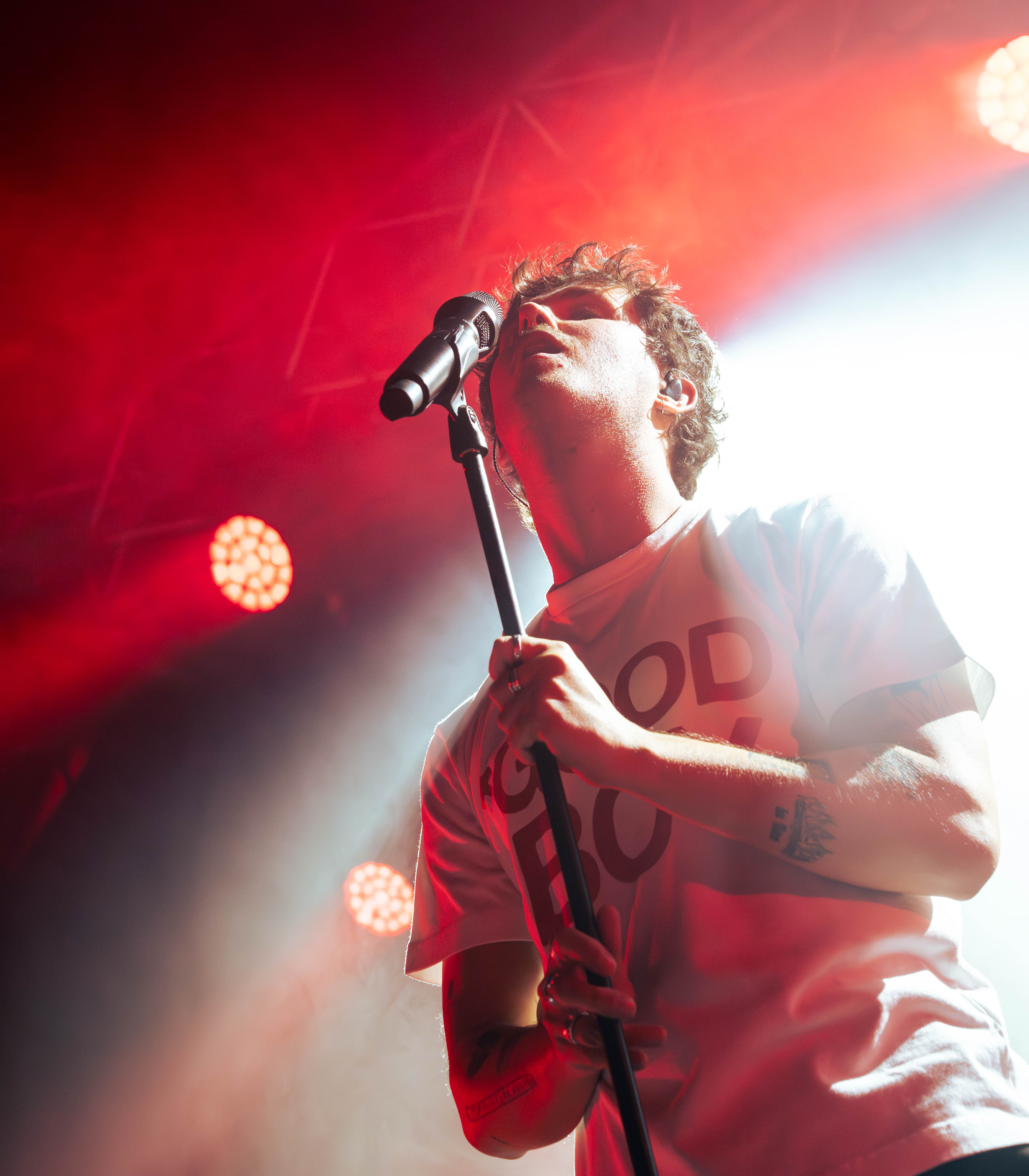 A musician performing passionately on stage with a microphone, illuminated by vibrant red and white lights.