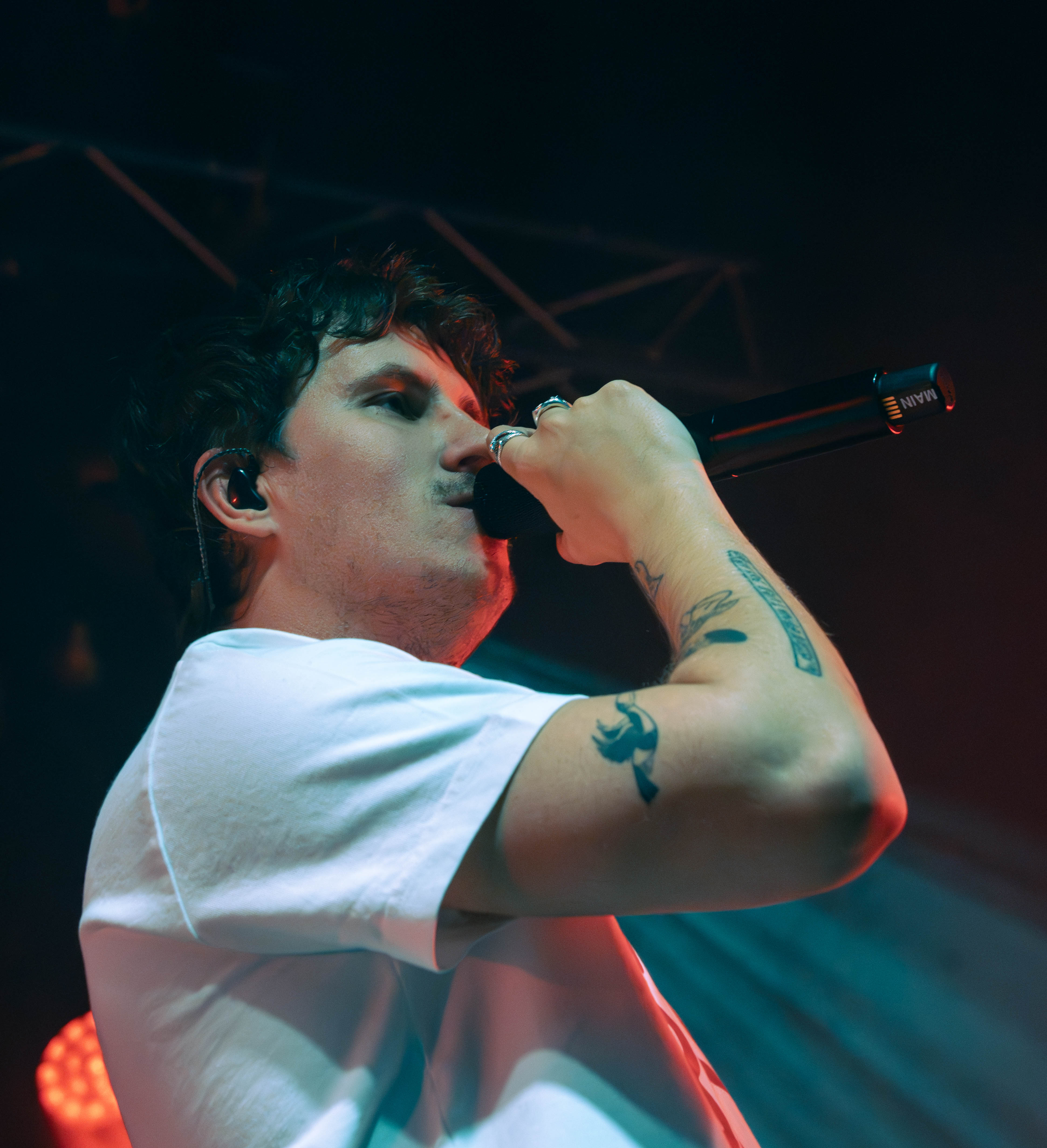 Close-up of a male singer holding a microphone, performing on stage with a dramatic lighting backdrop.