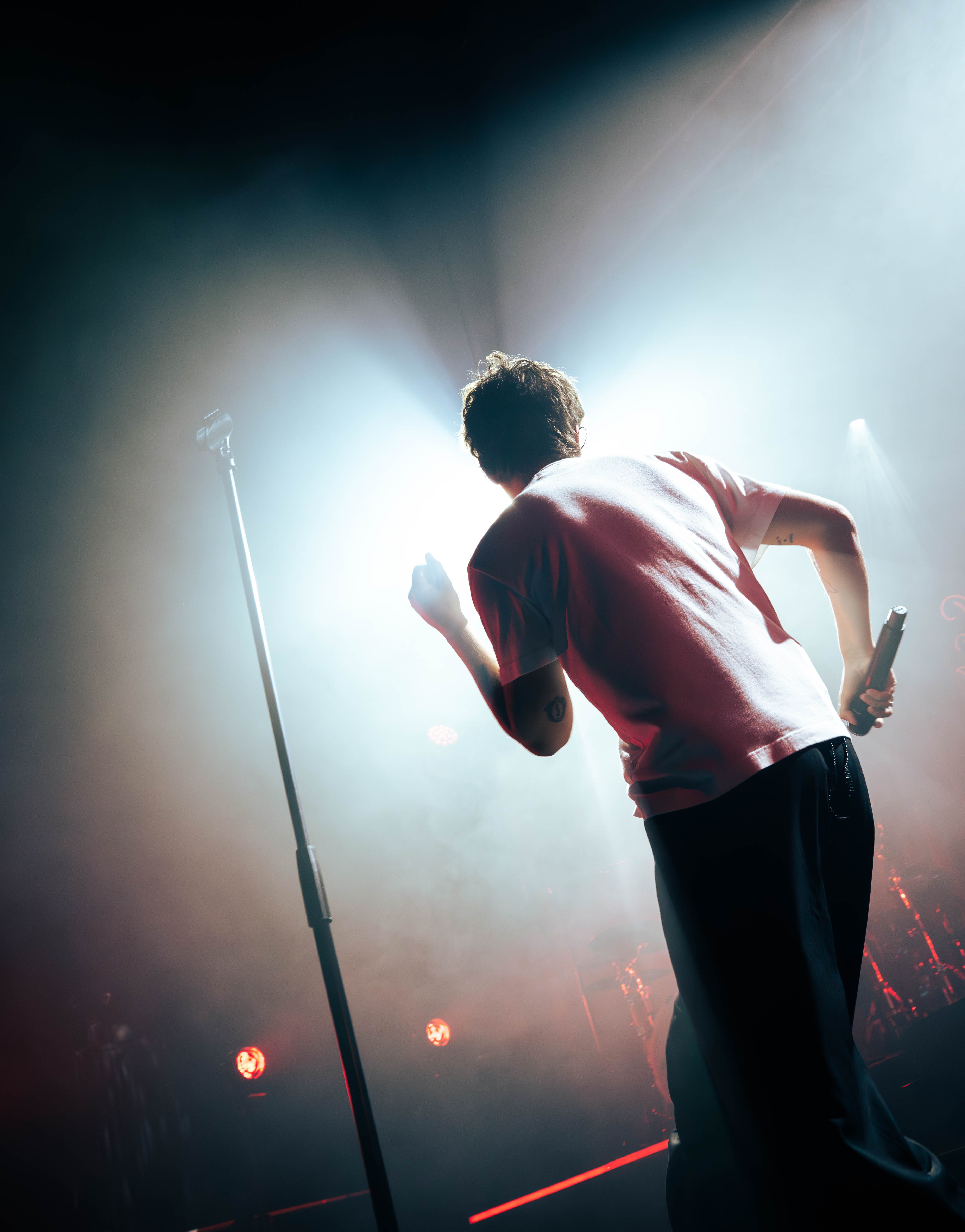 A musician performing on stage with a microphone stand in the foreground, illuminated by bright lights and surrounded by smoke.