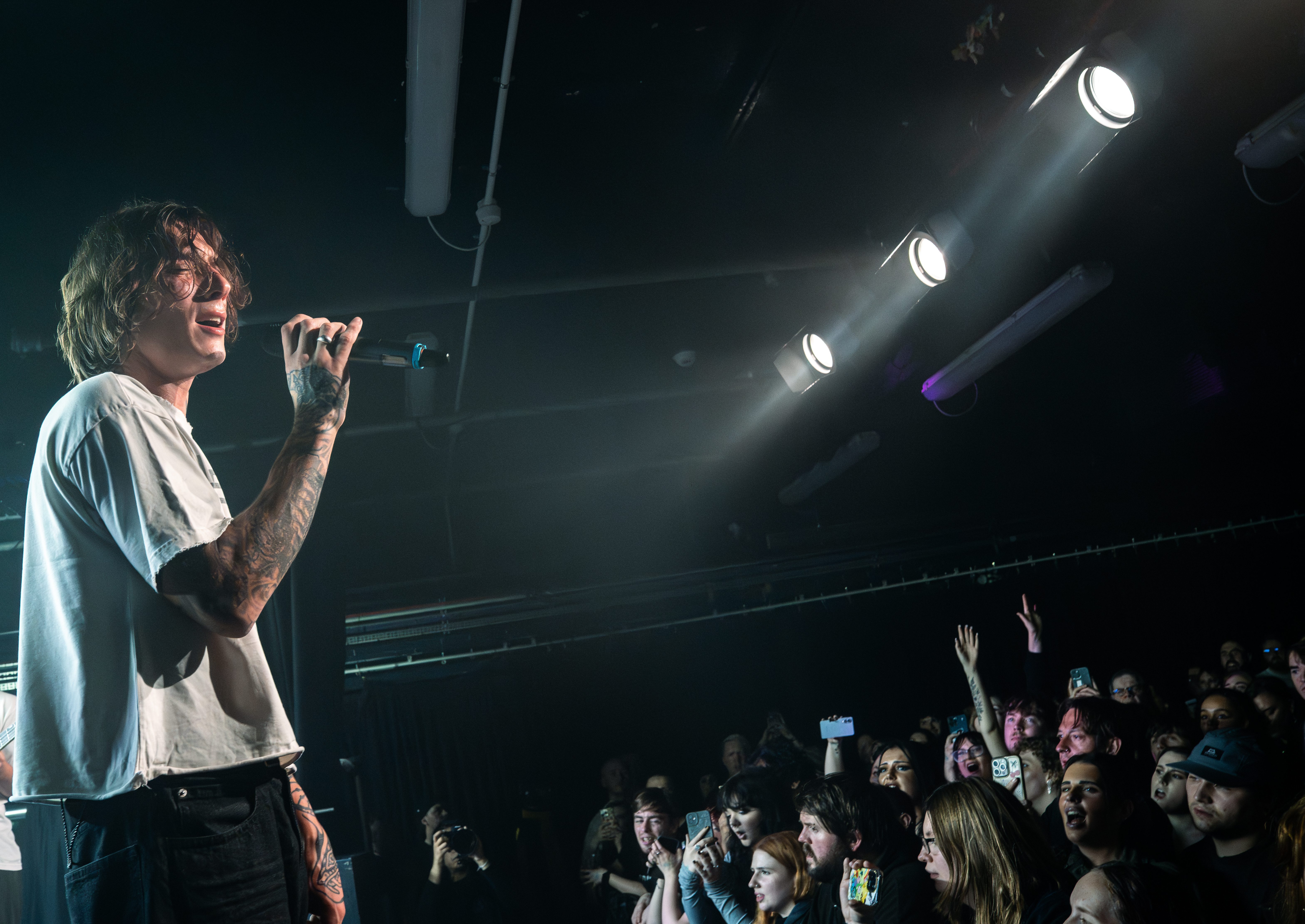 A musician performing on stage, holding a microphone while engaging with an enthusiastic crowd in a dimly lit venue.