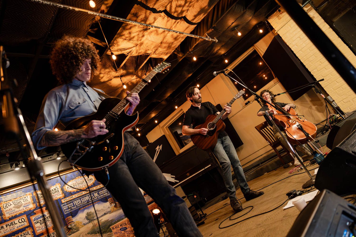 Live performance at Anodyne Coffee featuring musicians playing guitars and cello, with an intimate atmosphere and warm lighting.