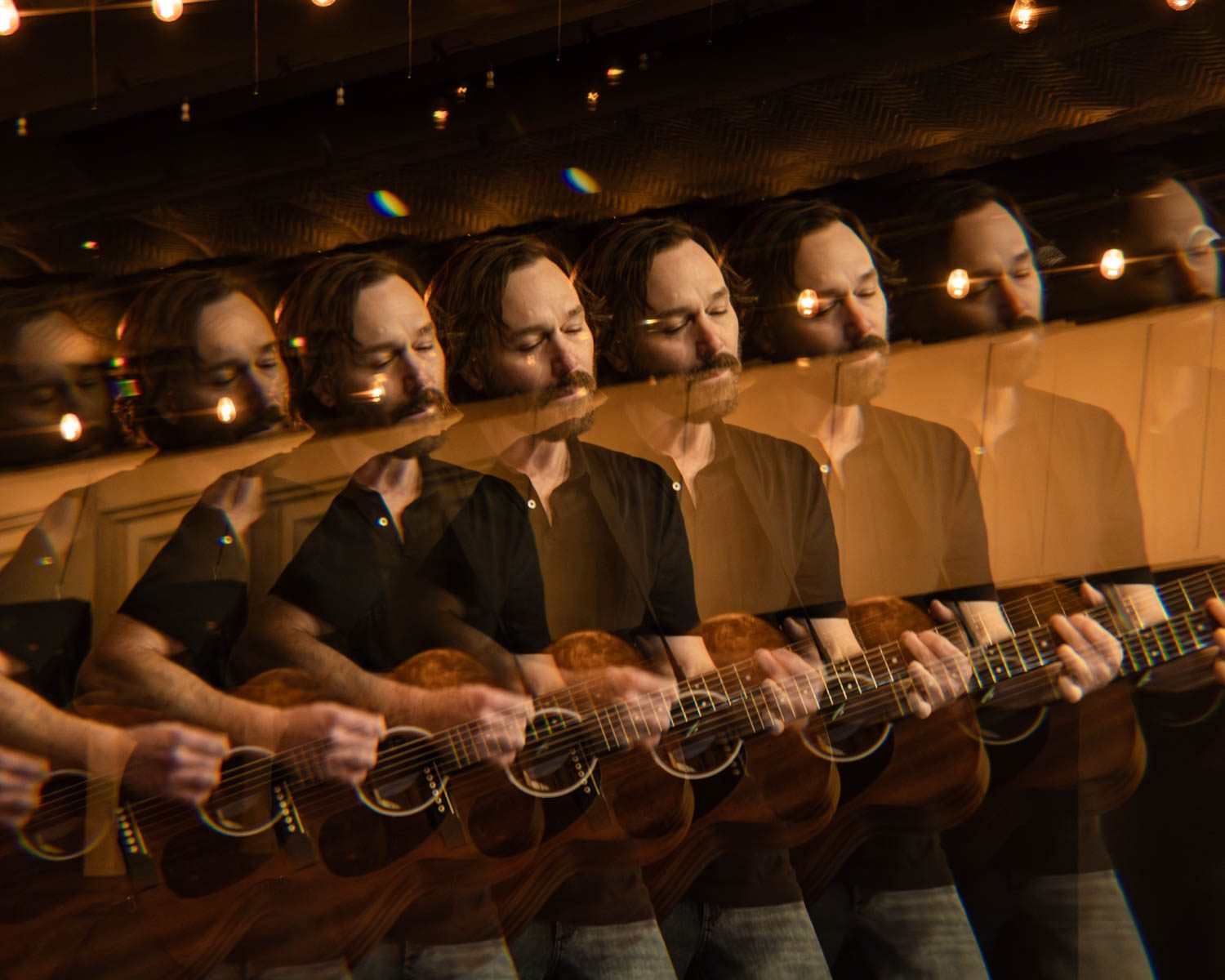 A blurred image of a musician playing an acoustic guitar, with multiple overlays creating a ghosting effect, in a cozy indoor setting with warm lighting.