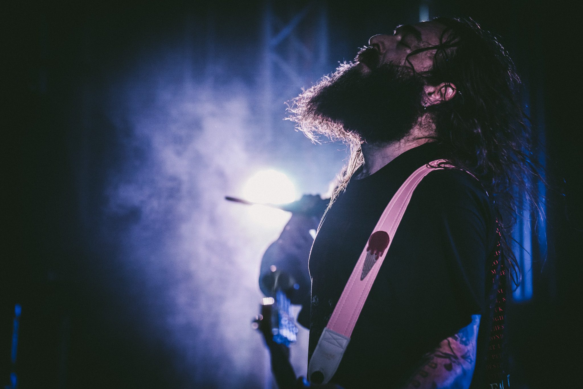 A confident man in a gray blazer poses with arms crossed in front of a blurred outdoor background.